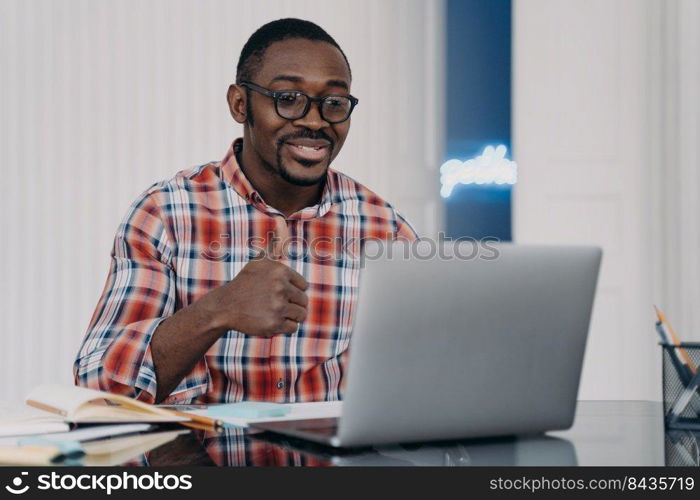 African american young man showing thumb up gesture looking at laptop. Black guy student wearing glasses shows like sign, talking with friend by video call online, gives positive feedback.. African american man shows like or thumb up gesture communicates online at laptop. Positive feedback