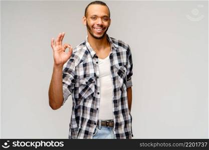 african-american young man wearing casual shirt and showing ok sign over light grey background.. african-american young man wearing casual shirt and showing ok sign over light grey background
