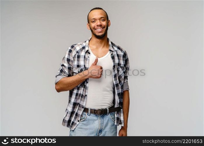 african-american young man wearing casual shirt and showing thumbs up over light grey background.. african-american young man wearing casual shirt and showing thumbs up over light grey background