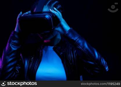 African-American young woman in vr glasses watching 360 degree video with a virtual reality headset isolated on a black background in neon light