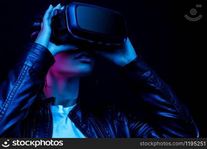African-American young woman in vr glasses watching 360 degree video with a virtual reality headset isolated on a black background in neon light
