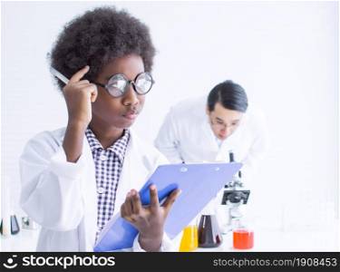 African black little boy wearing eyeglasses, studying science in classroom at school and thinking of something with blur background of teacher. Education concept.