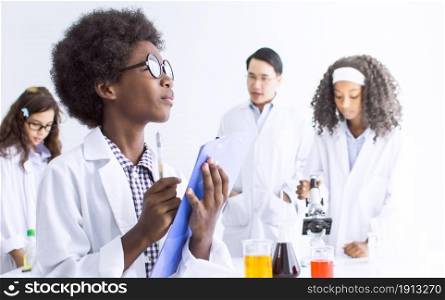 African black little boy wearing eyeglasses, studying science in classroom at school and thinking of something with blur background of teacher. Education concept.