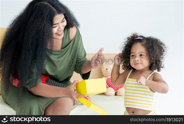 African black mother with afro hair giving gift box to her little daughter in living room at home for celebrating birthday. Education and Family Concept.