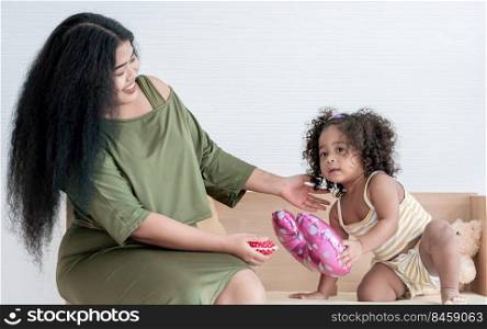 African black mother with afro hair playing ukulele with her little daughter in living room at home. Education and Family Concept.