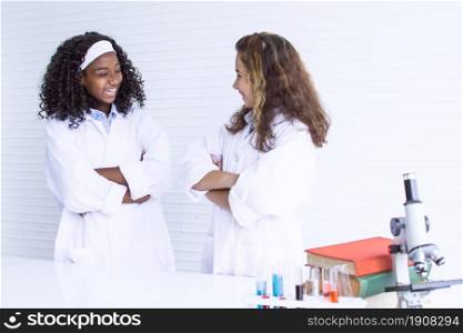 African black teen girl and caucasian white girl lauging and smiling to each other while studying science in classroom. Education and Diversity concept.