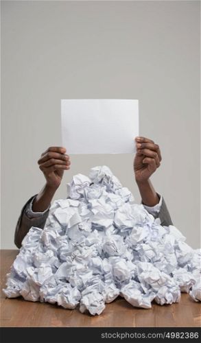 African business woman under crumpled pile of papers with raised hand holding a blank sign