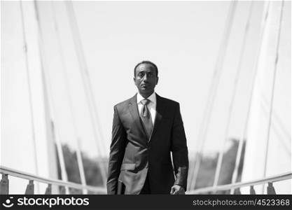 african businessman walking across modern bridge