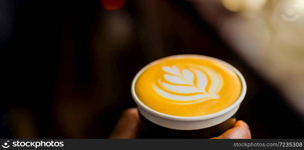 African Coffee Barista holding a take away cup with milk foam in a leaf shape