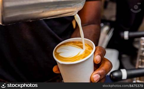 African Coffee Barista pouring a heart shape design with milk foam 