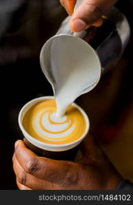 African Coffee Barista pouring a leaf shape with milk foam in a take away cup