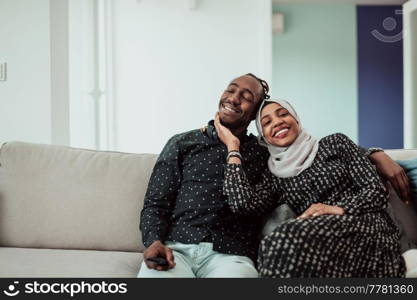African Couple Sitting On Sofa Watching TV Together. Women Wearing Islamic Hijab Clothes. High-quality photo. African Couple Sitting On Sofa Watching TV Together. Woman Wearing Islamic Hijab Clothes