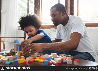 African family Dad and son sitting playing game at home together. Happy Black Father and kid boy building tower of colourful wood blocks toy. Development, Learning and Education concept.