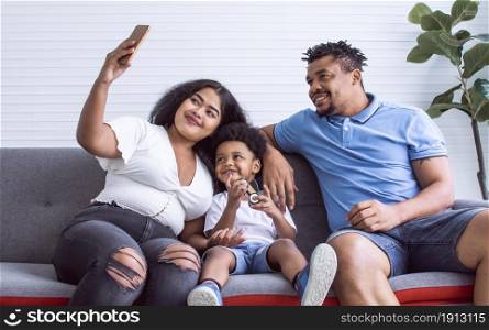 African family taking selfie by using mobile phone and sitting on sofa at home. Lifestyle Concept.