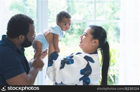 African father and Asian beautiful mother carrying cute newborn baby up in the air, playing and looking at infant with love and care at home. Multiracial family and child care concept