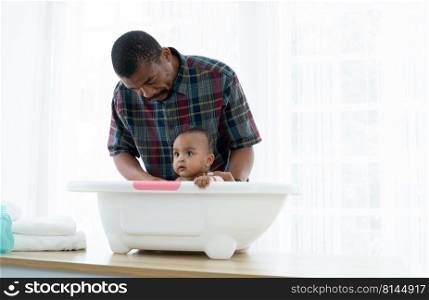 African father with beard bathing adorable newborn baby daughter in bathtub at home. Dad clean and wash his little toddler kid in warm water. Newborn baby hygiene cleanliness care concept