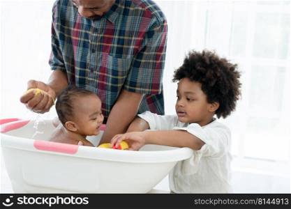 African father with beard bathing adorable newborn baby daughter in bathtub with sponge at home. Child boy help dad cleaning and playing with little sister in bath. Kid hygiene and care with family