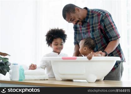 African father with beard bathing adorable newborn baby daughter in bathtub with sponge at home. Child boy help dad cleaning his little sister in bath. Kid hygiene and cleanliness care with family