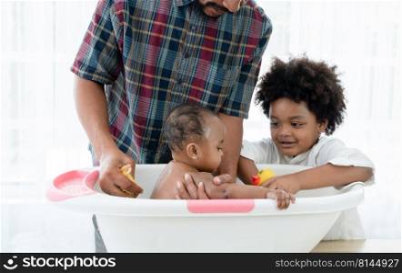 African father with beard bathing adorable newborn baby daughter in bathtub with sponge at home. Child boy help dad cleaning and playing with little sister in bath. Kid hygiene and care with family