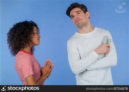 African girl asks her boyfriend for money for her whims, beauty salon and shopping. Husband reluctantly counts her dollar bills. Interracial couple concept. Blue studio background. High quality photo. African girl asks her boyfriend for money for her whims, beauty salon and shopping. Husband reluctantly counts her dollar bills. Interracial couple concept. Blue studio background.