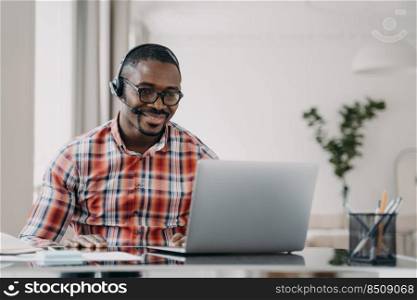 African male student wearing headset distance learning language online at laptop sitting at desk at home. Black guy wears headphone watching webinar, listening lecture. E-learning, remote education.. African american male student wearing headset learn language online at laptop. Distance education
