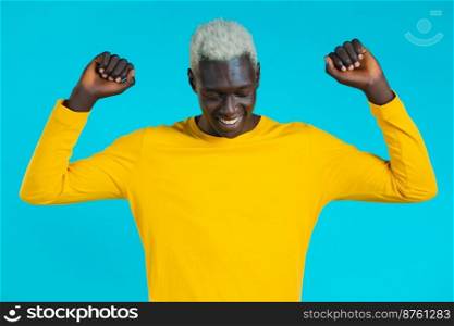 African man dancing positive on blue studio background. Handsome male afro black model guy in yellow. Party, happiness, freedom, youth concept. African man dancing positive on blue studio background. Handsome male afro black model guy in yellow. Party, happiness, freedom, youth concept.
