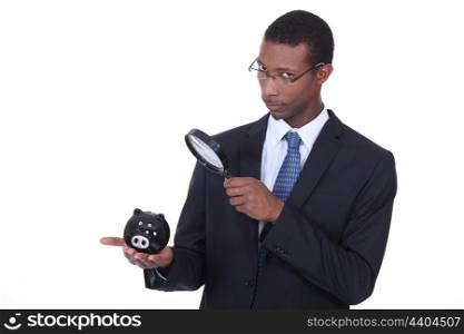 African man looking at a piggy bank through a magnifying glass