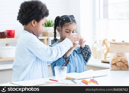 African siblings, brother giving little sister a glass of milk to drink in kitchen at home. Adorable boy looking after of child girl with love and care after playing, drawing together. Family bond