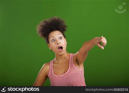 African woman astonished with something and pointing, over a green background