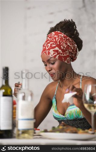 African woman eating at home and drinking wine and looking very happy
