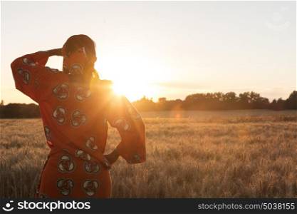 African woman in traditional clothes looking across a field of barley or wheat crops at sunset or sunrise