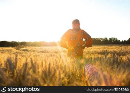 African woman in traditional clothes standing in a field of barley or wheat crops at sunset or sunrise