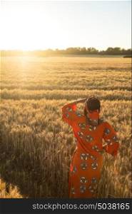 African woman in traditional clothes standing looking across a field of barley or wheat crops at sunset or sunrise