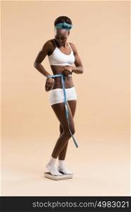 African woman standing on scale measuring waist with tape celebrating weightloss and a healthy fit body