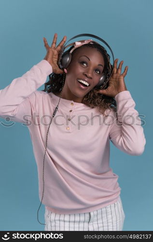 African woman with headphones listening music. Music teenager girl dancing against blue background