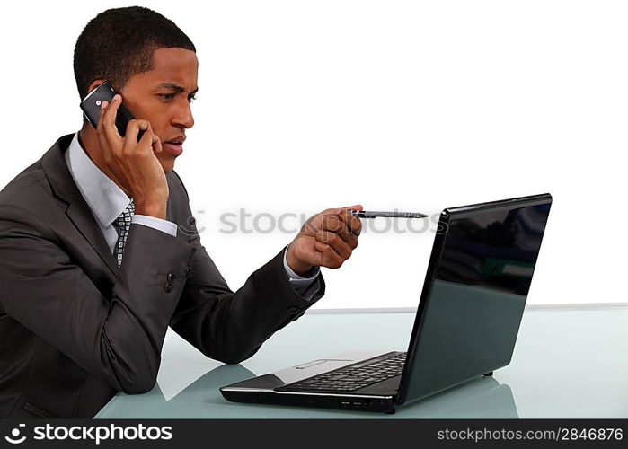 Afro-American businessman looking at his laptop and talking on the phone