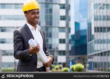 Afro american construction engineer in front of building holding blueprints