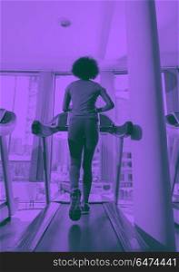 afro american woman running on a treadmill. afro american woman running on a treadmill at the gym while listening music on earphones duo tone filter