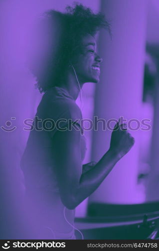 afro american woman running on a treadmill. afro american woman running on a treadmill at the gym while listening music on earphones duo tone filter