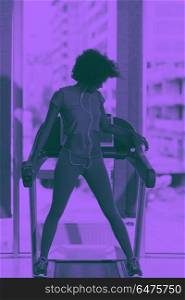afro american woman running on a treadmill. afro american woman running on a treadmill at the gym while listening music on earphones duo tone filter