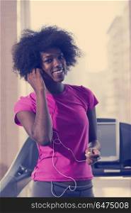 afro american woman running on a treadmill at the gym while listening music on earphones. afro american woman running on a treadmill