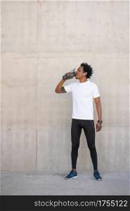 Afro athletic man drinking water and relaxing after work out outdoors. Sport and healthy lifestyle concept.