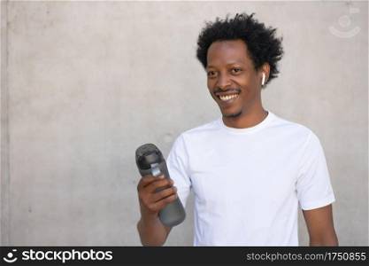 Afro athletic man holding a bottle of water and relaxing after work out outdoors. Sport and healthy lifestyle.