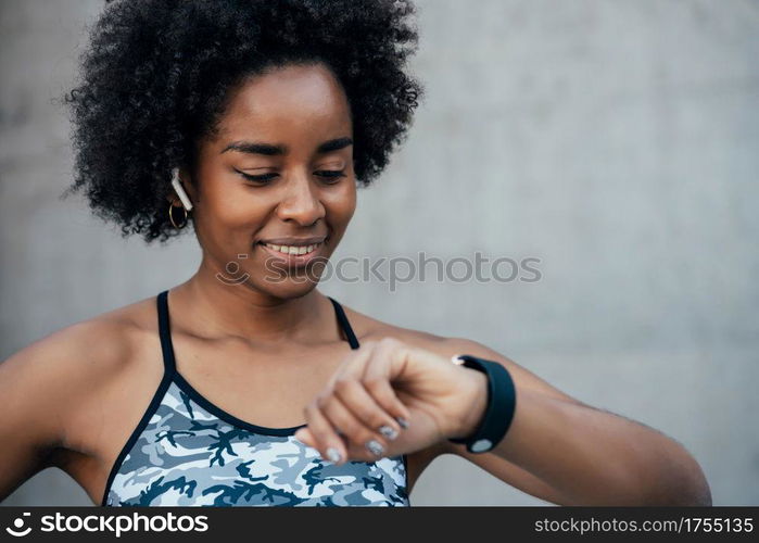 Afro athletic woman checking time on her smart watch while work out outdoors. Sport and healthy lifestyle concept.