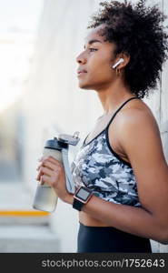 Afro athletic woman drinking water and relaxing after work out outdoors. Sport and healthy lifestyle concept.