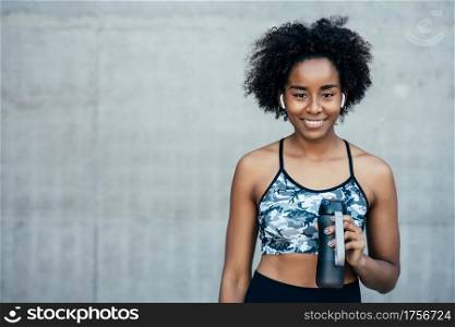 Afro athletic woman drinking water and relaxing after work out outdoors. Sport and healthy lifestyle.