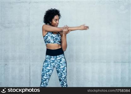 Afro athletic woman stretching her arms and warming up before exercise outdoors. Sport and healthy lifestyle concept.