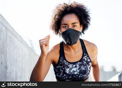 Afro athletic woman wearing face mask while running outdoors. New normal lifestyle. Sport and healthy lifestyle concept.