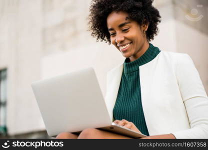 Afro business woman using her laptop while sitting on stairs outdoors. Urban and business concept.. Business woman using her laptop outdoors.