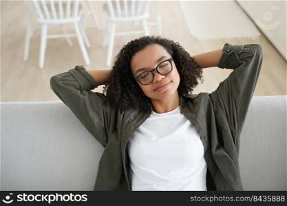 Afro girl naps on sofa. Attractive african american girl is relaxing on couch at home with her hands under head. Young woman is smiling with her eyes closed. Comfort and cosy home concept.. Afro girl naps on sofa. African american girl relaxing on couch at home with her hands under head.